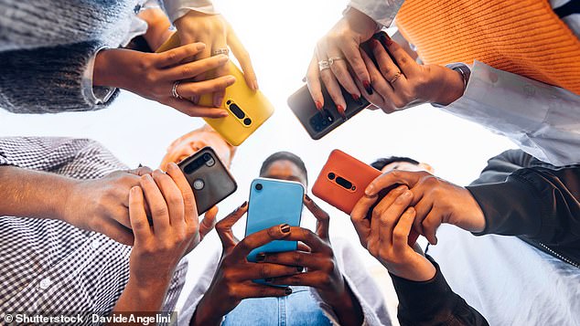 Teenagers gather in a circle on their phones. Growing up surrounded by technology has damaged attention spans (stock image)