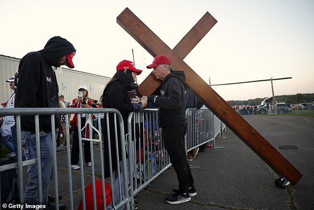 Don Deazley carries a cross as he prays with Sue Hensal and others as they wait in line for a rally of Republican presidential candidate, former U.S. President Donald Trump, at the Butler Farm Show Inc. on October 5, 2024 in Butler, Pennsylvania