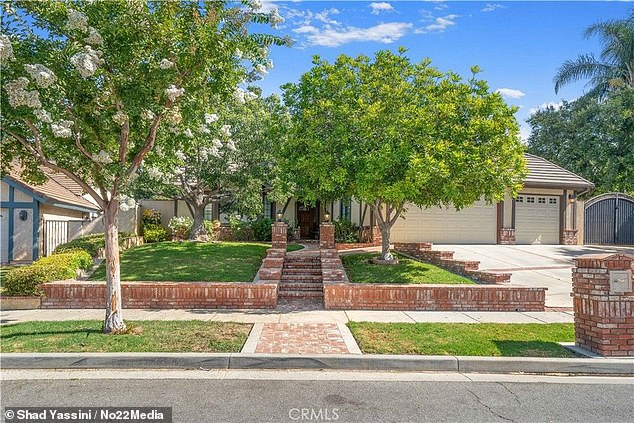 The front of the house has a three-car garage, as well as areas of green grass and a few shady trees - while a stone walkway leads to the wooden front door.