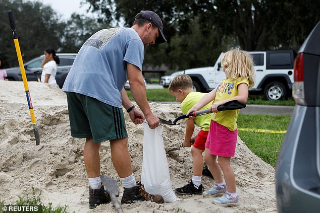 Tom Murphy prepares a sandbag with children as sandbags are distributed to Pinellas County residents ahead of the expected arrival of Tropical Storm Milton on Sunday in Seminole, Florida