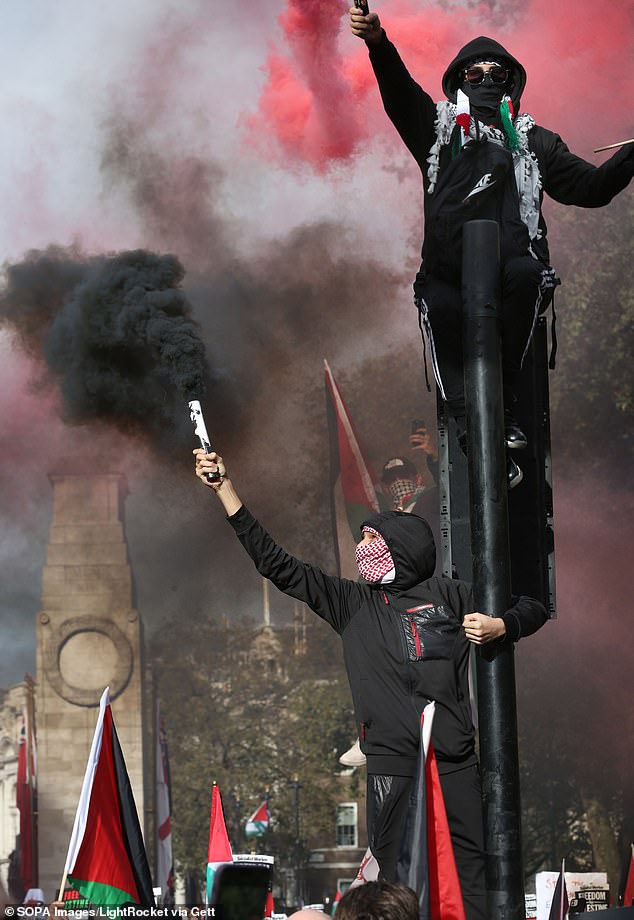 Pro-Palestinian protesters hold smoke flares as they cling to a traffic light outside Downing Street