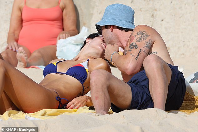 The pair relaxed on the sand after their ocean swim and could barely keep their hands off each other