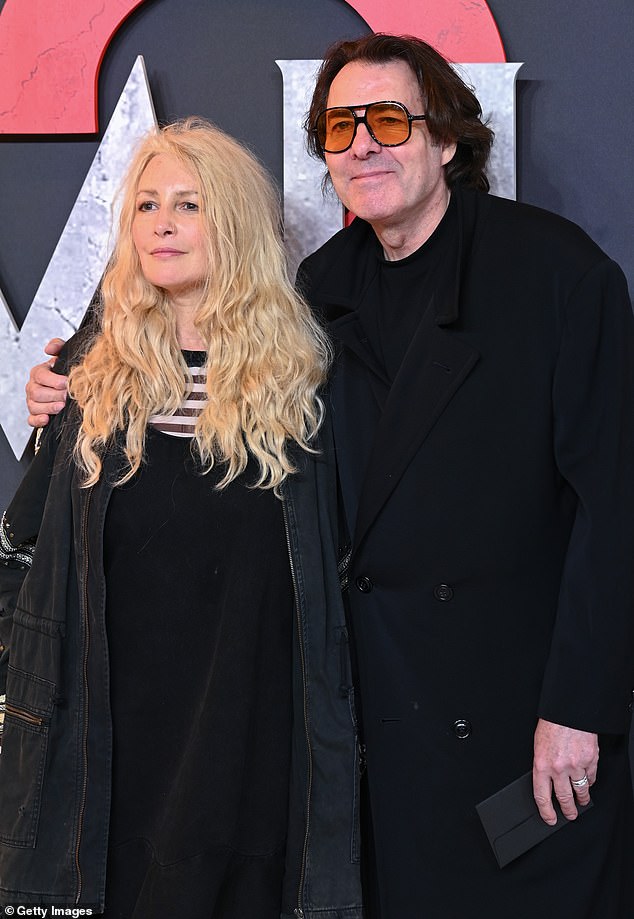 Jonathan wore a black dress coat and orange tinted glasses as he affectionately wrapped his arm around his wife