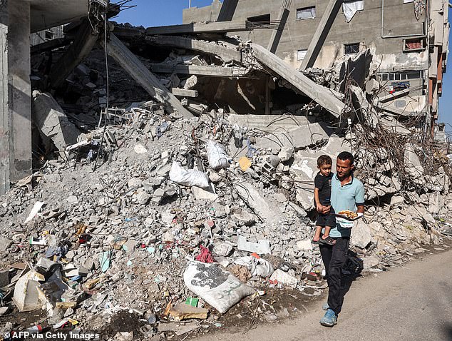 A man carries a child as he walks past a collapsed building in the Bureij camp for Palestinian refugees in the central Gaza Strip on October 9