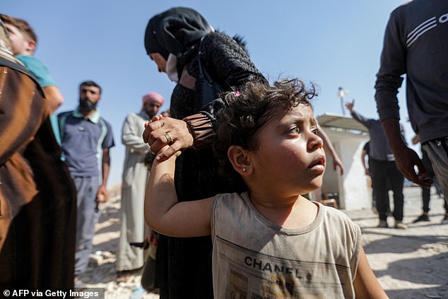 A woman holds the hand of a child as Syrians who were refugees in Lebanon return to their homeland after traveling to the opposition in the northern province of Idlib through the Aoun al-Dadat border crossing north of Manbij, on October 9, 2024