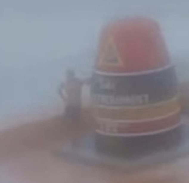 A man poses for a photo with the Southernmost Point buoy in Key West as the iconic landmark was battered by rain and high winds on Wednesday