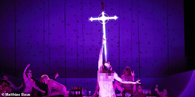 In one scene, tattooed naked performers clamber across a table, drinking wine and singing, while another lifts a sword in the shape of a crucifix and shoves it into her throat.