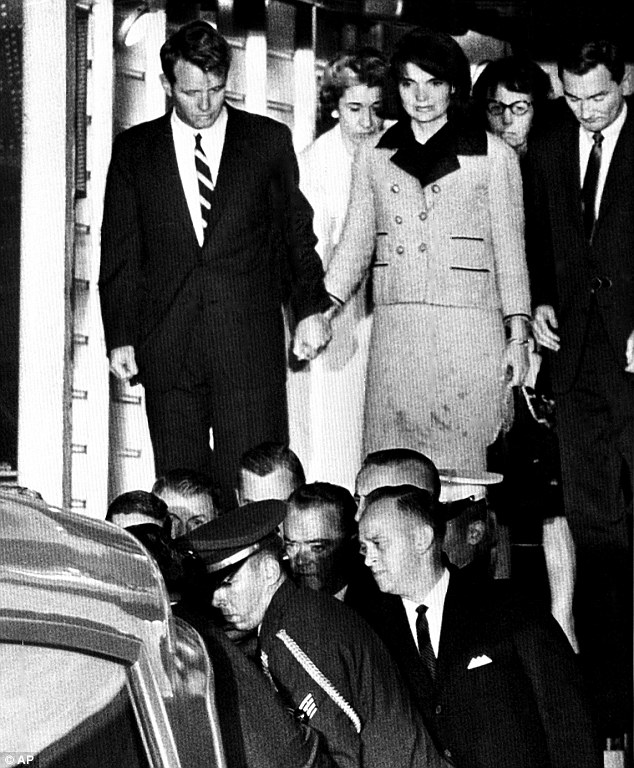 Jackie Kennedy grabs Bobby's hand as she stands, standing in her bloodstained clothes as the casket containing the body of President John F Kennedy is placed in an ambulance after arriving at Andrews Air Force Base