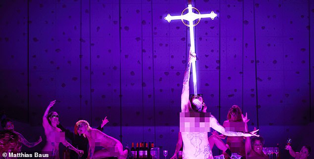 In one scene, tattooed naked performers clamber across a table, drinking wine and singing, while another lifts a sword in the shape of a crucifix and shoves it into her throat.