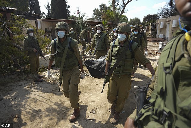 Israeli soldiers carry the body of a person killed in the Hamas attack in kibbutz Kfar Azza on Tuesday, October 10, 2023