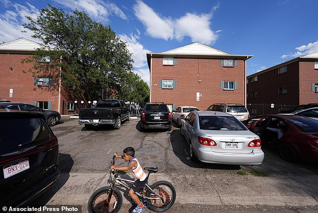 A boy guides his bicycle past apartment buildings as a courtyard meeting is held to address chronic problems in the apartment buildings occupied by people displaced from their homelands in Central and South America in Aurora