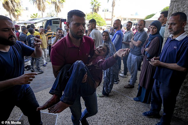 A Palestinian man carries an injured child after an Israeli airstrike in Deir al Balah