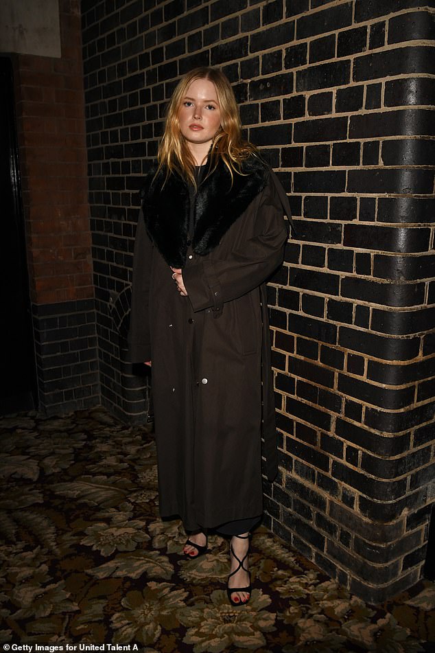 Ellie Bamber dressed up for the event in a dark brown coat with a black faux fur collar that she wore over a black dress