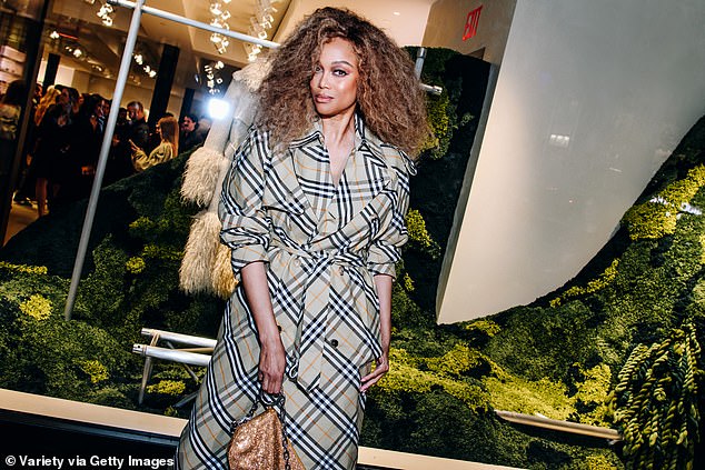 Tyra's long checked trench coat was a rejection of Burberry's trendy shorter coats of recent years. She wore it with long white slippers and carried a handbag with gold sequins