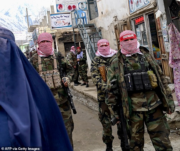 The alleged massacre comes after the Iranian regime's crackdown on migrants trying to escape the clutches of the Taliban. Pictured: Taliban security personnel stand guard as an Afghan woman wearing a burqa (right) walks down a street at a market in the Baharak district of Badakhshan province on February 26, 2024