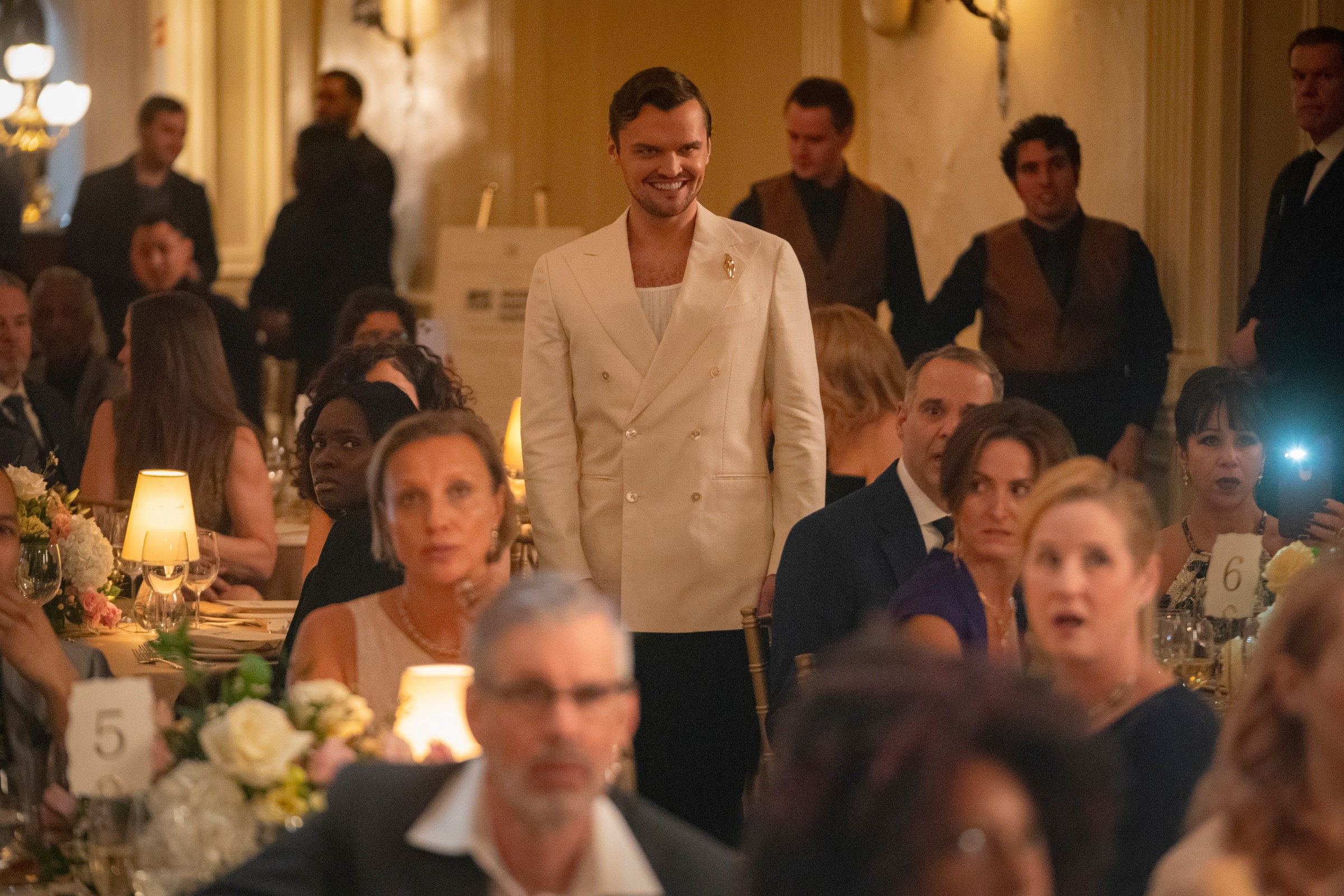 Ray Nicholson stands up at a black tie event, wearing a white jacket and a sinister grin on his face in Smile 2 