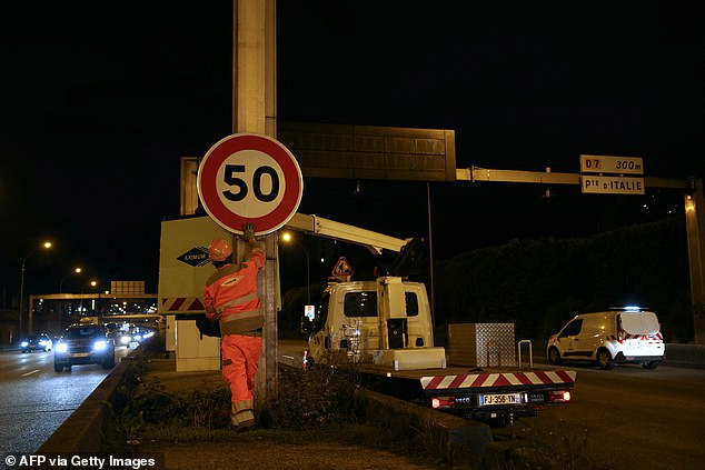 Construction workers place a sign with a speed limit of 50 km/h on the Paris ring road, the boulevard peripherique