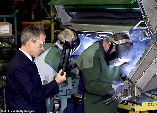 Former U.S. President George W. Bush (L) watches welders work on a John Deere combine during a factory tour on January 14, 2002 in Moline, Illinois