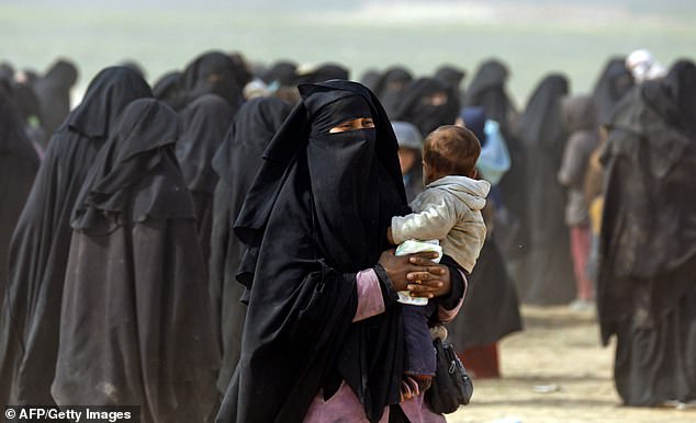 A fully veiled woman holds her baby as civilians fleeing the embattled Islamic State group Baghouz walk through a field on February 13, 2019