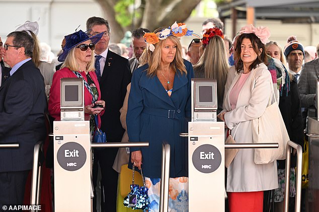 A group of women wearing fascinators and winter coats over their dresses waited patiently at the turnstiles