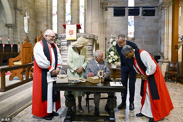 King Charles signs a copy of the Bible as Queen Camilla looks on during a visit to St. Thomas' Anglican Church