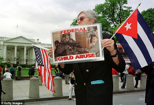 A member of Mothers Against Repression holds a photo of a federal agent with an automatic rifle confronting fisherman Donato Dalrymple holding Elian Gonzalez in a closet during a demonstration outside the White House April 26, 2000 Washington, D.C.