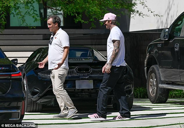 Beckham is pictured wearing a pink Inter Miami hat, white T-shirt and black trousers