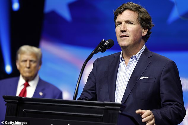 Political commentator Tucker Carlson speaks alongside Republican presidential candidate, former US President Donald Trump, during a Turning Point Action campaign rally