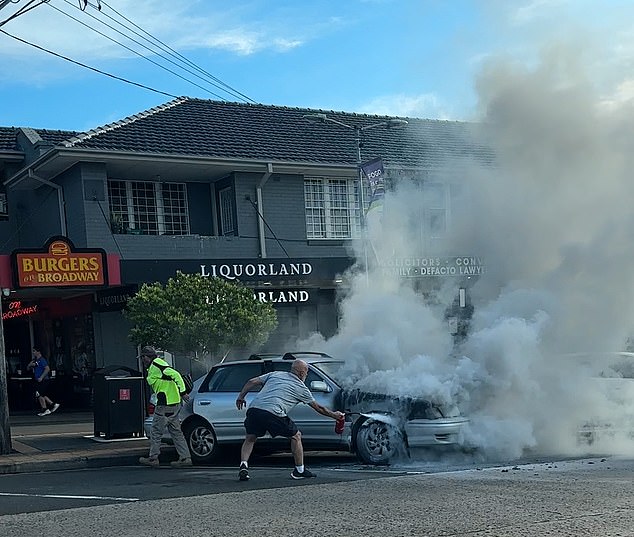 A heroic man rushes to the inferno with a small fire extinguisher to try to put out the flames without much success