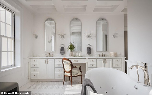 One of the bathrooms has three sleek silver mirrors with an all-white interior to the cabinets, freestanding bath and floors. It has a large square glass shower