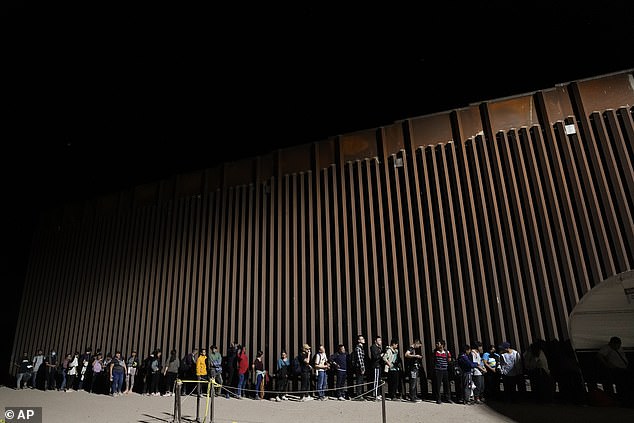 People line up against a border wall as they wait to seek asylum after crossing the border from Mexico on Tuesday, July 11, 2023, near Yuma, Arizona. Thousands of migrants from the North African country of Mauritania have arrived in the US in recent months, following a new route that takes them to Nicaragua and across the southern border.