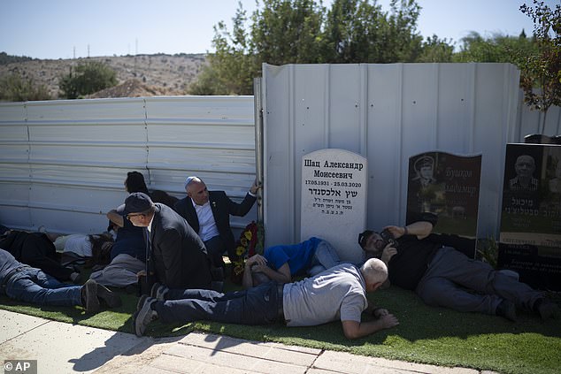 People take cover as a siren warns of incoming missiles during the funeral of Alexei Popov, who was killed in a rocket attack fired from Lebanon over the weekend, at the Tel Regev cemetery on the outskirts of Haifa, northern Israel, Monday October 21. 2024