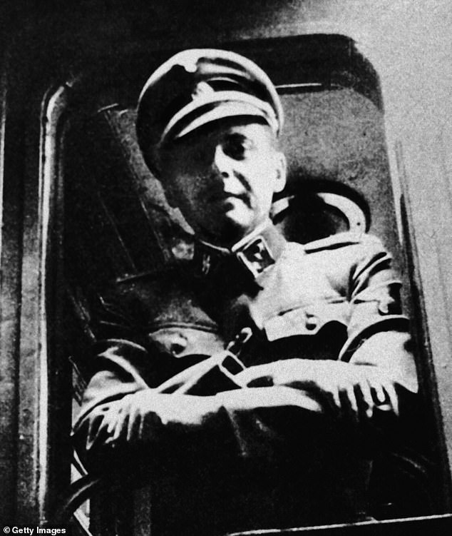 Mengele stands in front of a train window in his SS uniform