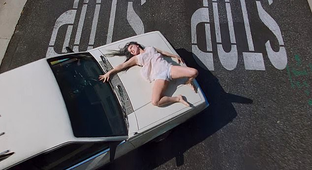 The video begins with the star apparently the victim of a car accident as she lies bloodied on the hood of a car