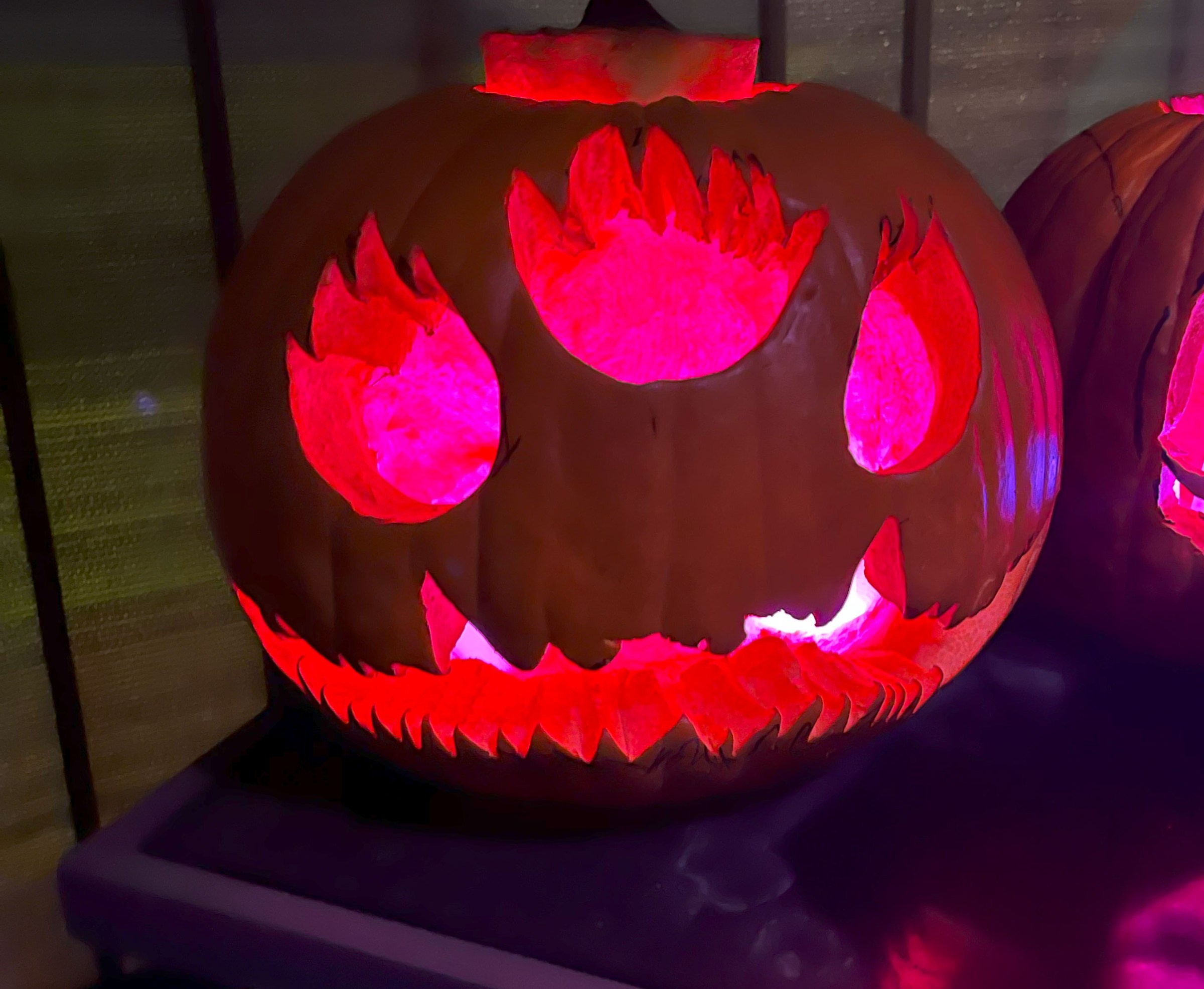 A jack-o-lantern with three eyes that resemble flames and a whimsical long mouth. The functions are illuminated with pink lights.