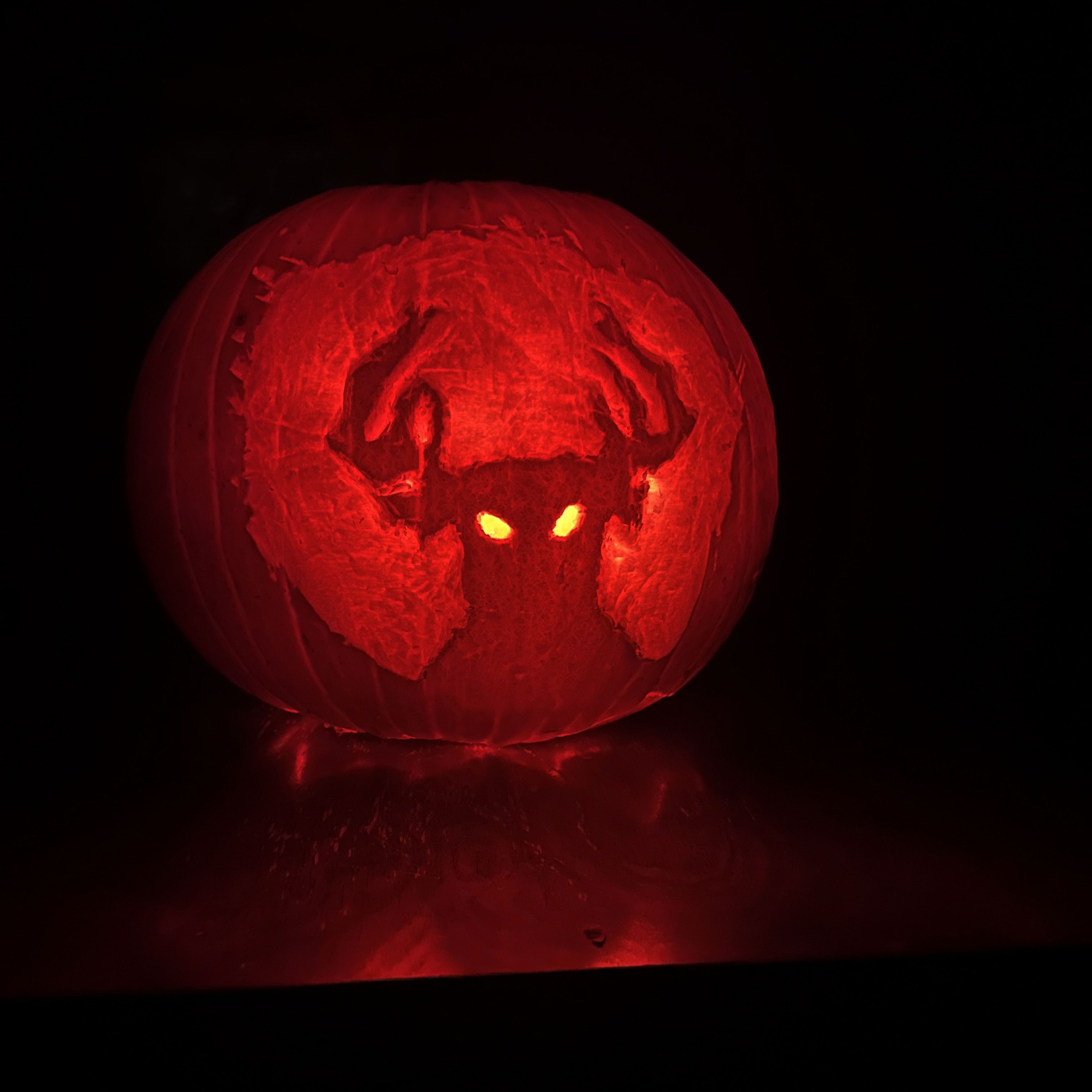 A pumpkin is carved with the silhouette of a person with moose horns and glowing eyes. The background lights up softly.  