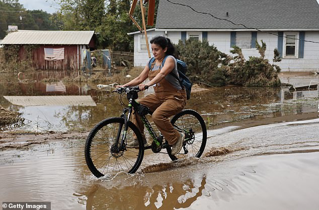 A person cycles through the water left after Hurricane Helene on October 4, 2024 in Swannanoa, North Carolina