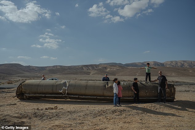 People take photos of and stand on the remains of a rocket in Israel