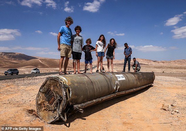 Children and adults stand atop the remains of an Iranian missile in the Negev Desert near Arad, Israel