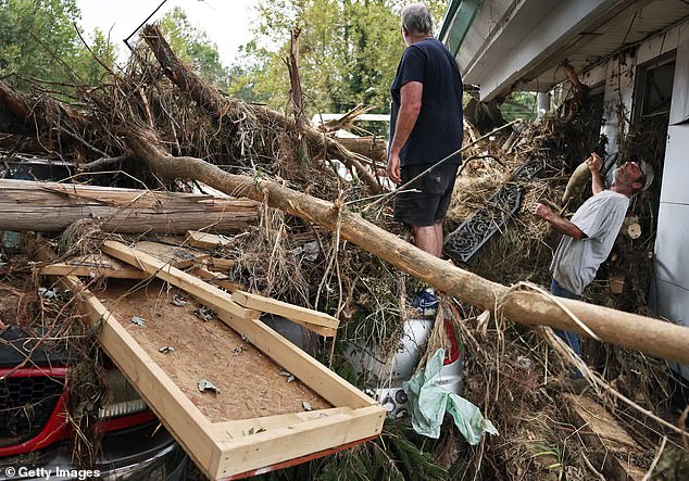 People clean up flood debris from Monteath's Auto Service in the aftermath of Hurricane Helene's flooding along the Swannanoa River on October 4, 2024 in Asheville, North Carolina. More than 220 people died as a result of the storm. The cleanup will cost tens of billions of dollars