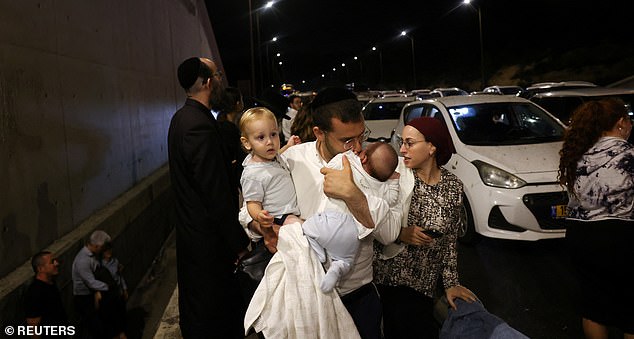 A man holds two children as people take cover during an air raid siren in Israel