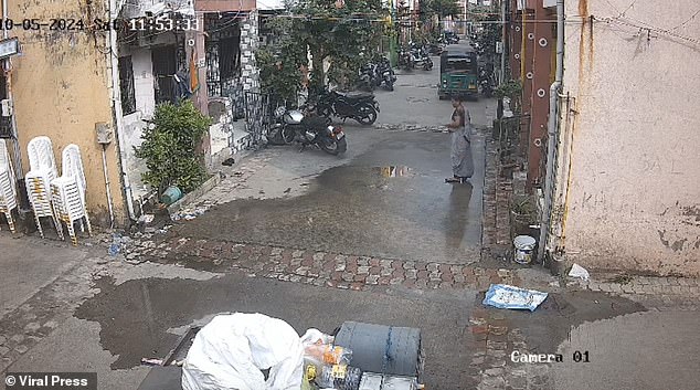 The video shows the woman crossing a narrow road while eating a piece of fruit, when the large tank suddenly came barreling towards her from above