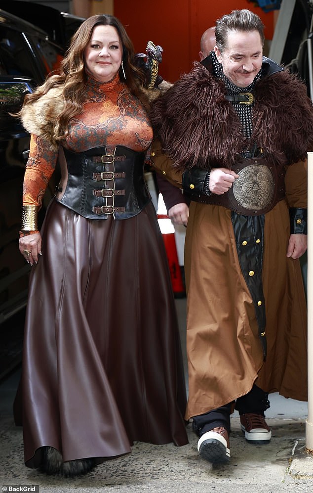 Melissa McCarthy showed off her sexy new curves wearing a black and brown viking costume with corsets on Live with Kelly and Mark Tuesday. She and husband Ben Falcone dressed up to promote their latest project, the Hildy the Barback and the Lake of Fire podcast