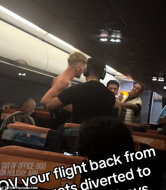 Another passenger, wearing a black T-shirt and headphones, appears to be trying to de-escalate