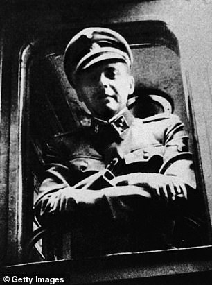 Mengele stands in front of a train window in his SS uniform