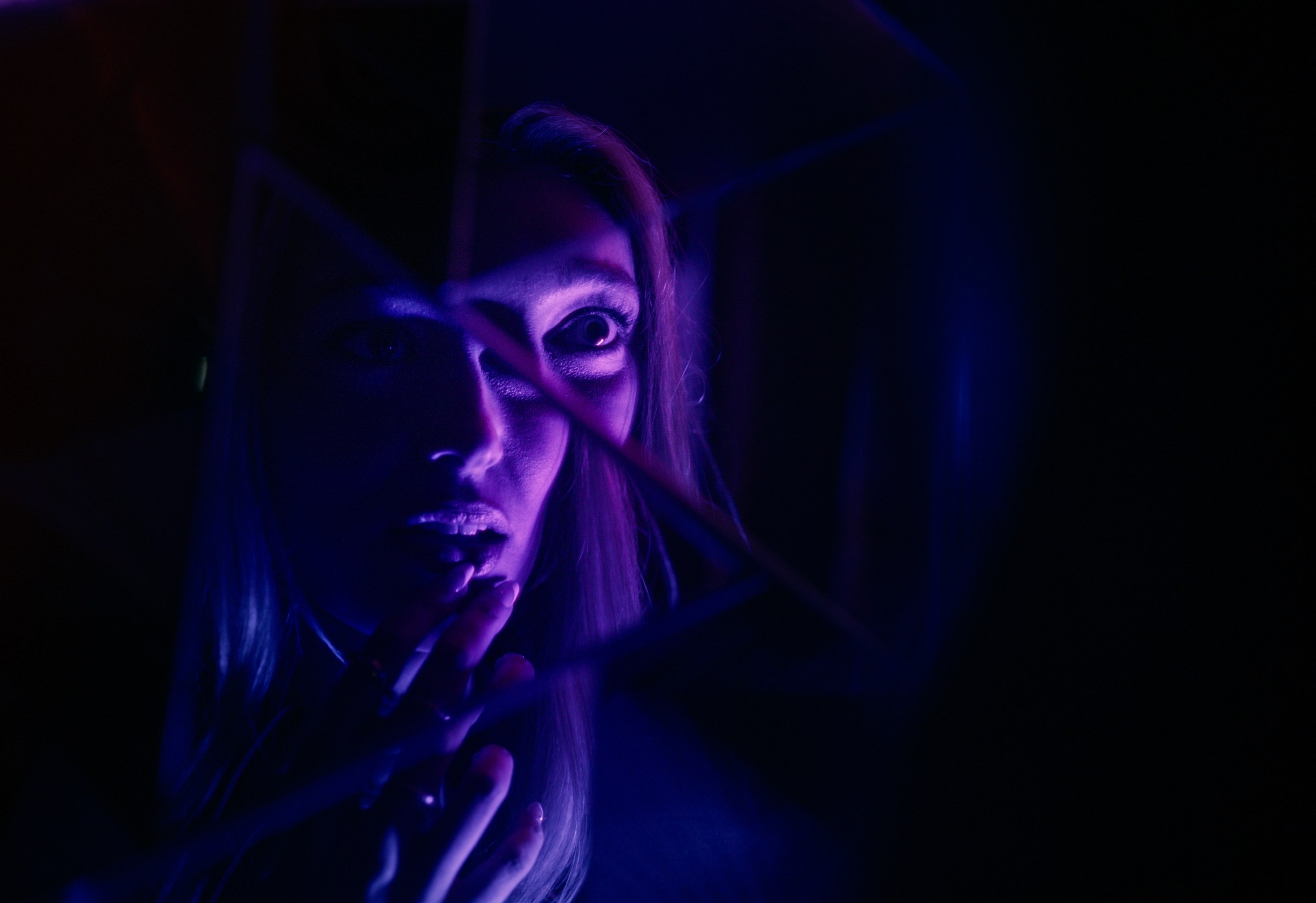 A woman, illuminated in purple light, looks into a fragmented mirror and applies lipstick. From the Netflix film It's What's Inside