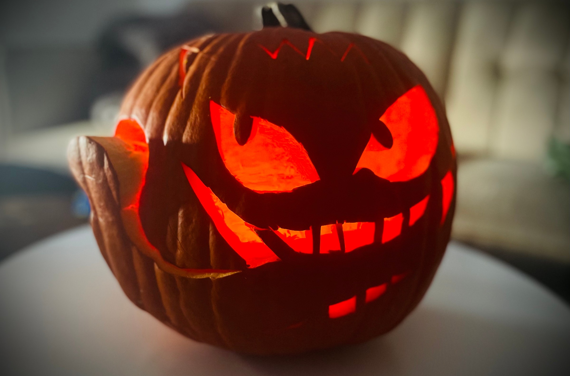 A jack-o'-lantern with cat-shaped eyes pointing in different directions and large teeth carved into its face. There is a piece of pumpkin cut out like a tongue that wraps around it.