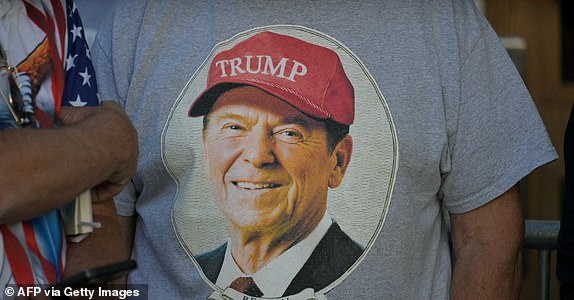 A man wears a t-shirt with a photo of former US President Ronald Reagan wearing a Trump hat as supporters line up for a rally with Republican presidential candidate, former US President Donald Trump, in the Santander Arena in Reading, Pennsylvania, on October 9, 2024 (Photo by Jim WATSON/AFP) (Photo by JIM WATSON/AFP via Getty Images)