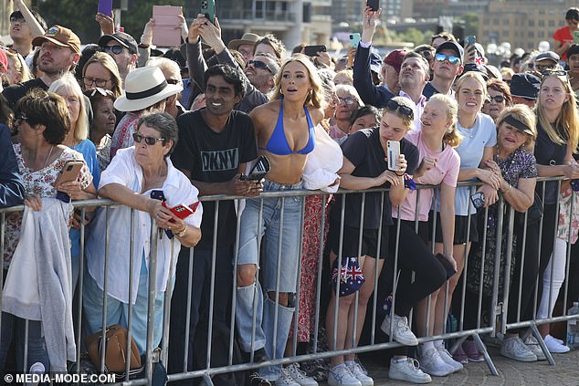 A bikini-clad young Australian woman (pictured centre) has shocked royal fans by holding a very provocative sign during King Charles' visit to the Sydney Opera House