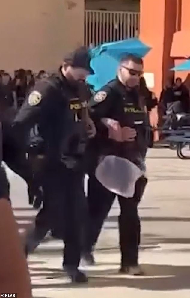 School district police officers carry the combative student as other students look on, stunned and bewildered